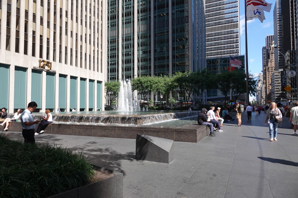 A group of people sitting on benches in front of the fountain.