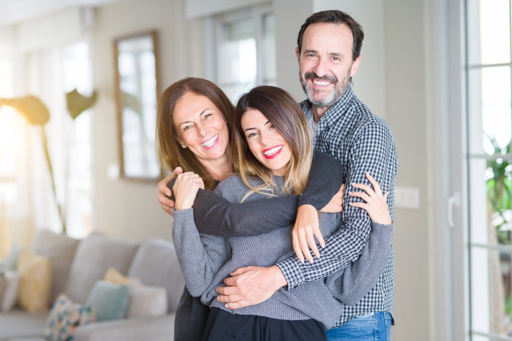 Happy family - mother, father and daughter hugging and smiling at home